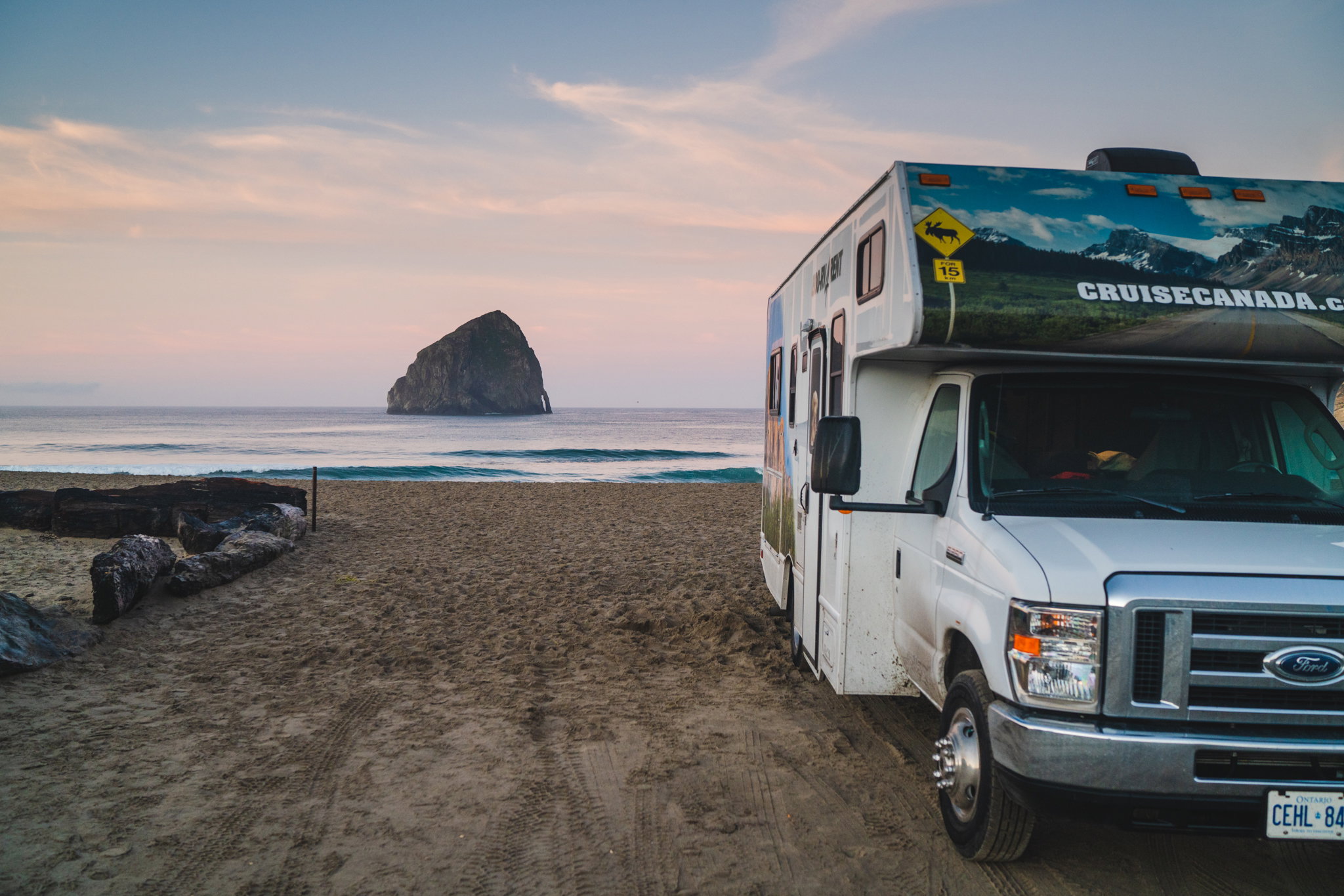 A Cruise Canada motorhome is parked up on the beach at sunset with purple and orange hues, Vancouver Island, British Columbia, Canada