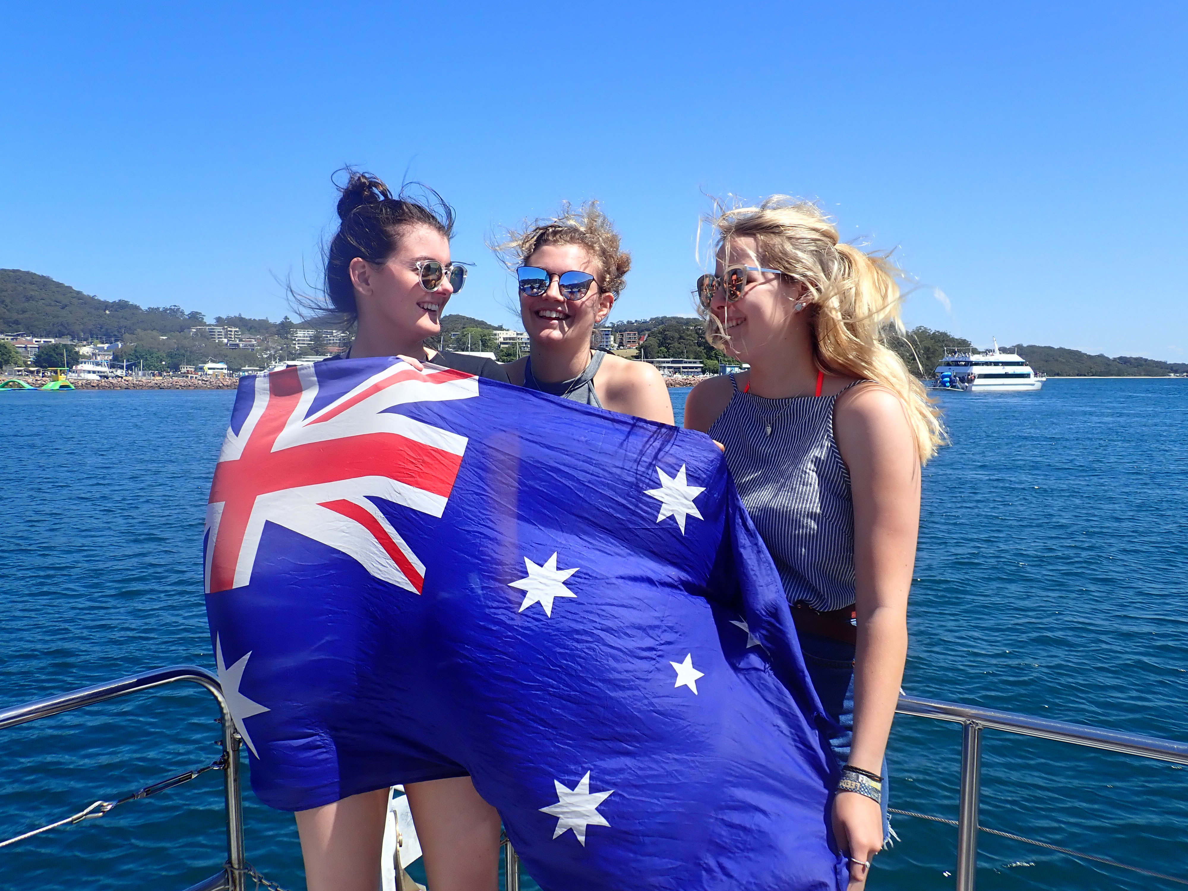 Three young travellers posing with the australian flag draped over them in New South Wales, Australia