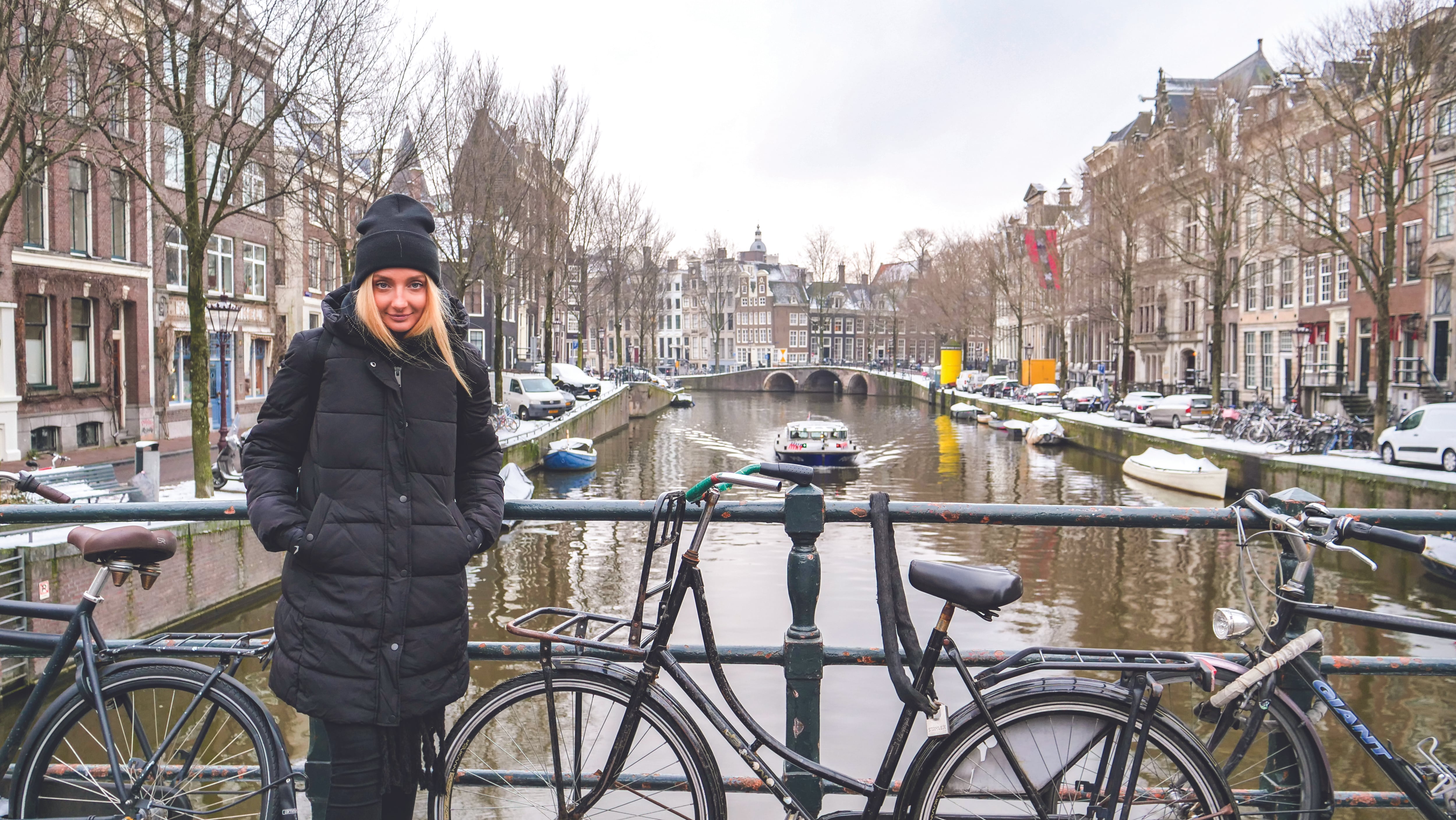 A lady poses in her winter coat in front of a row of bikes leaning against the railing next to the river Amstel on a cold winter's day in Amsterdam, Netherlands