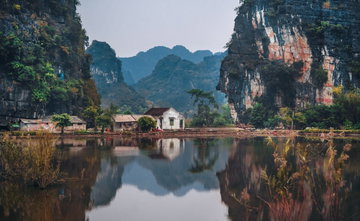 Ramshackle, tile roofed houses sit in the shadows of towering limestone pillars with trees and shrubs bursting from the cracks in Northern Vietnam