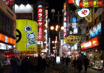 A nightime scene of a bustling Osaka street lit up with colourful neon lights, billboards and signs, Japan.
