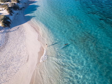 A aerial view of bright white sands and a couple swimming in Turqoise Bay, Ningaloo Reef, Western Australia