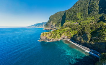 The deep blue Atlantic Ocean hugs the rocky Madeira coastline, covered in lush vegetation.