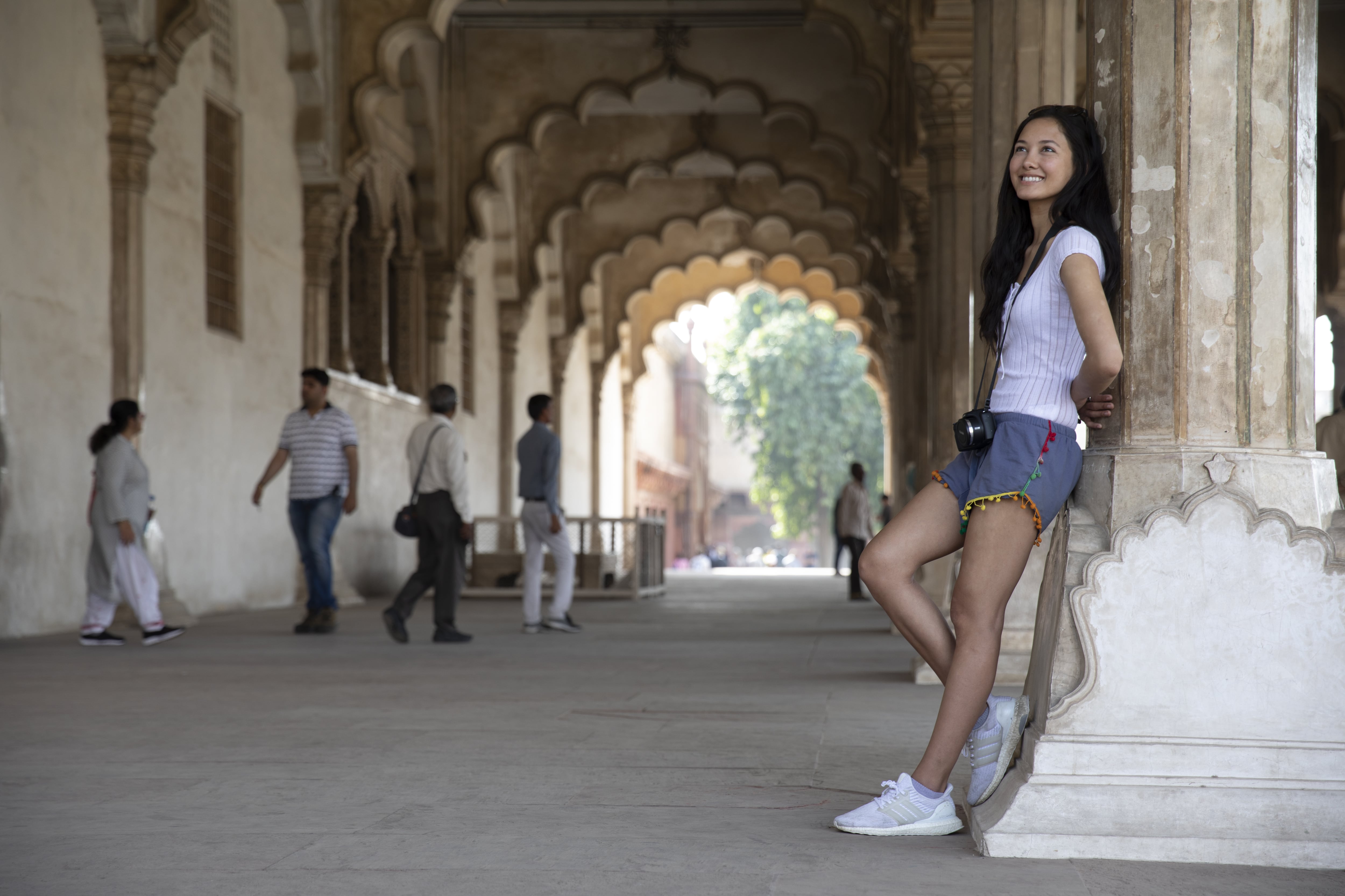 A female traveller with a camera around her neck leans against the wall in one of Agra's elaborate ancient archways