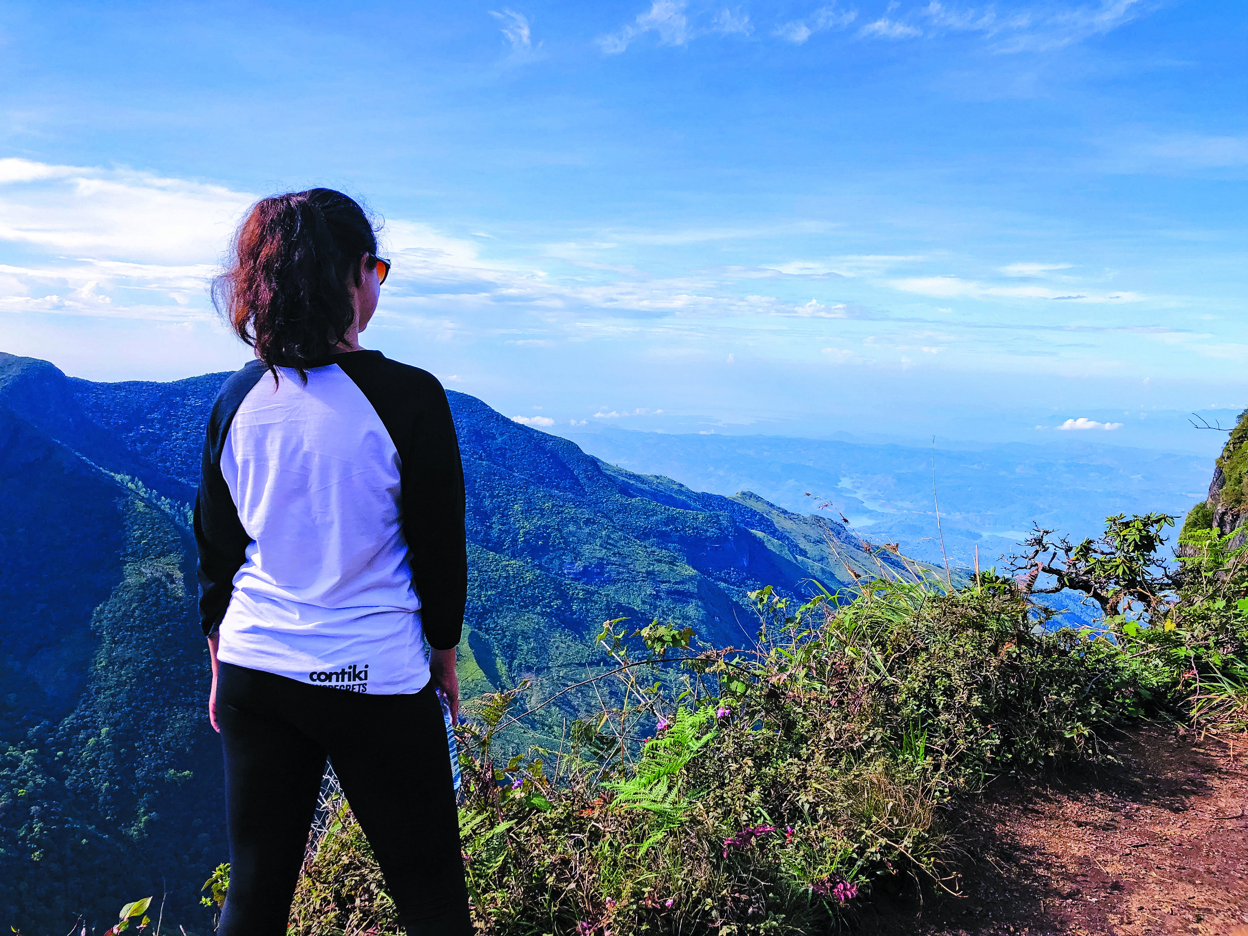 A female in a contiki branded top looks out over the lush countryside of Sri Lanka's tea country from a high viewpoint.