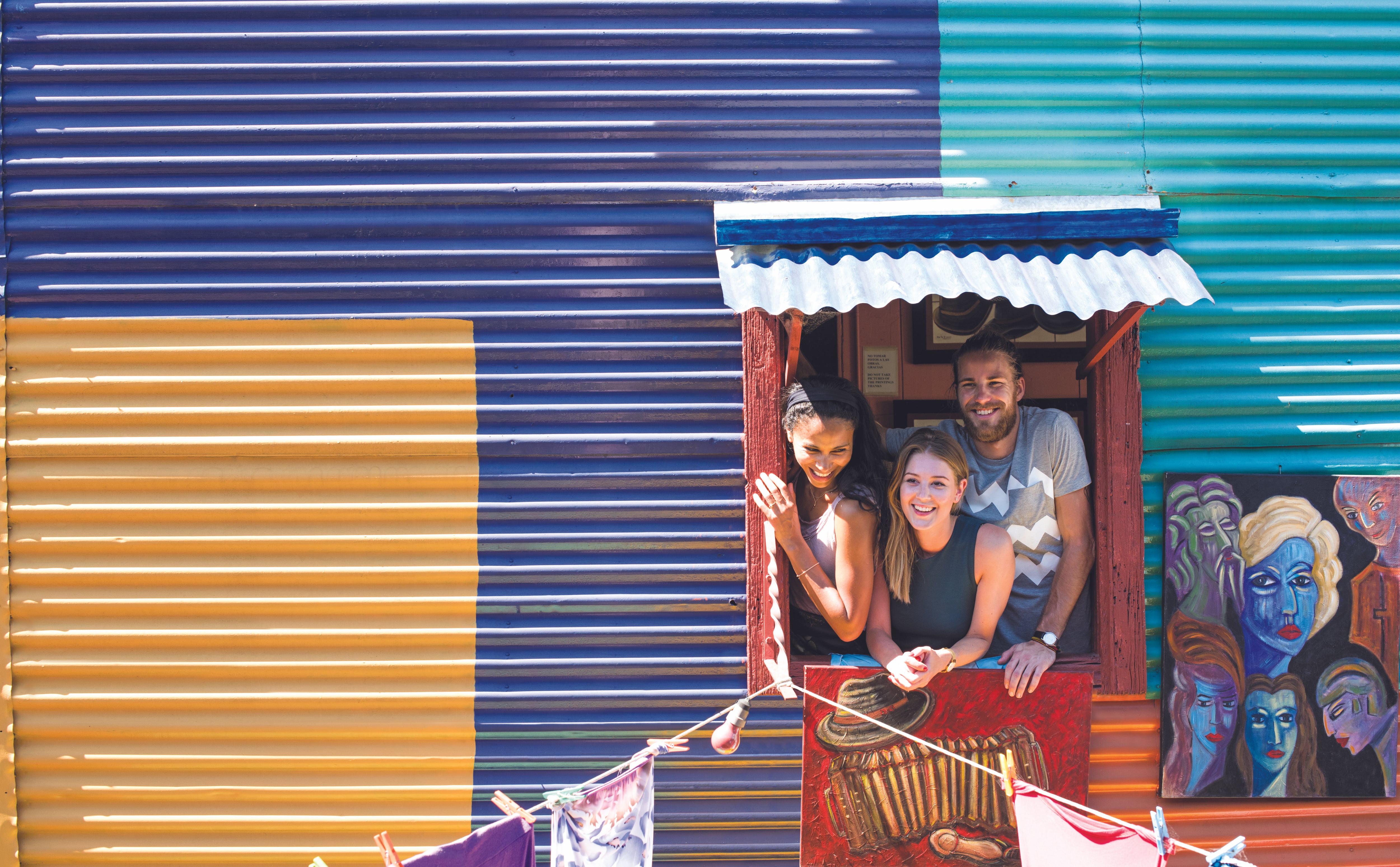 Three travellers poke their heads through the window of a Buenos Aires building made from multi-coloured corrugated metal