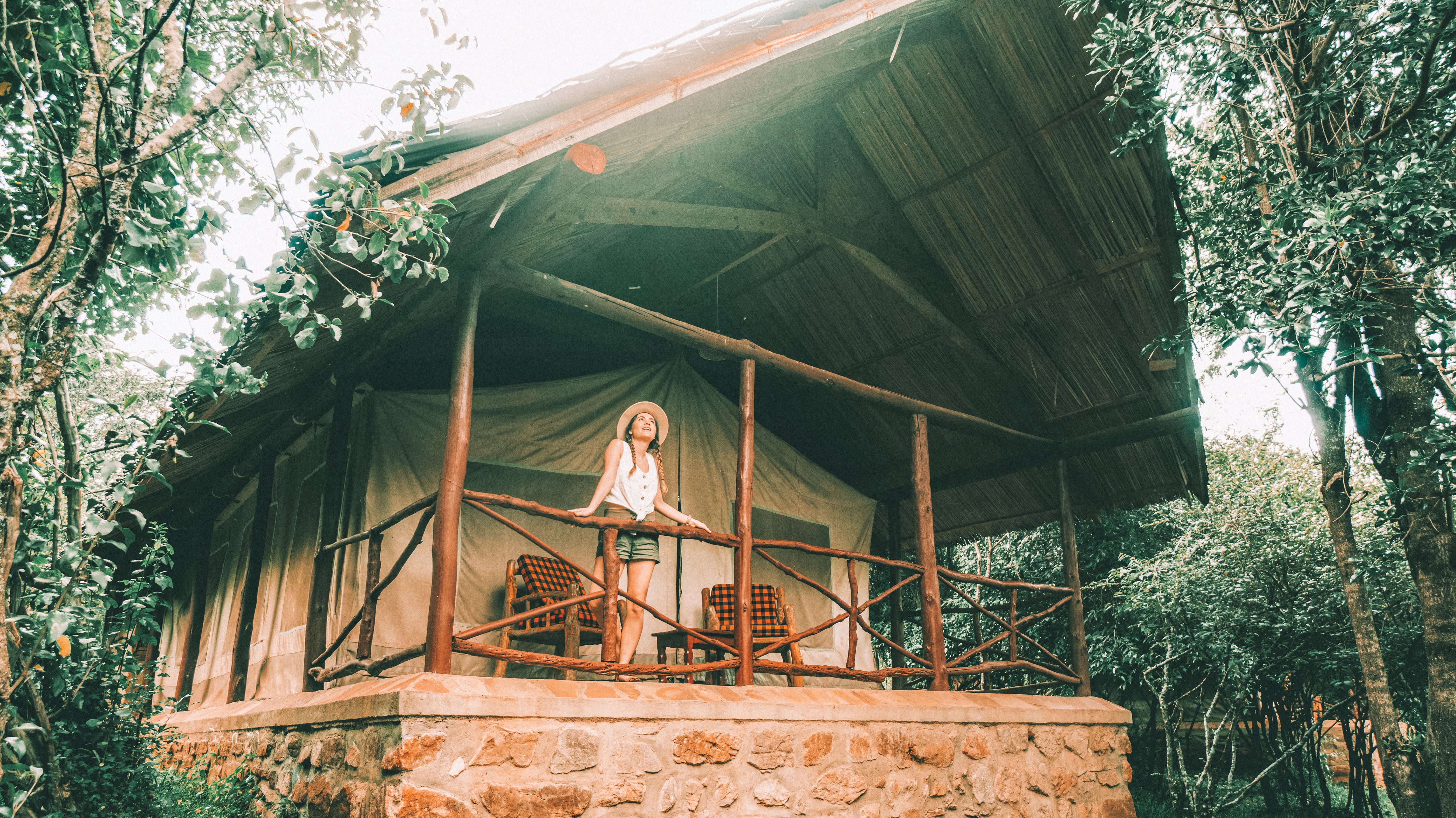 A female traveller in a sun hat leans on the verandah in front of her safari tent