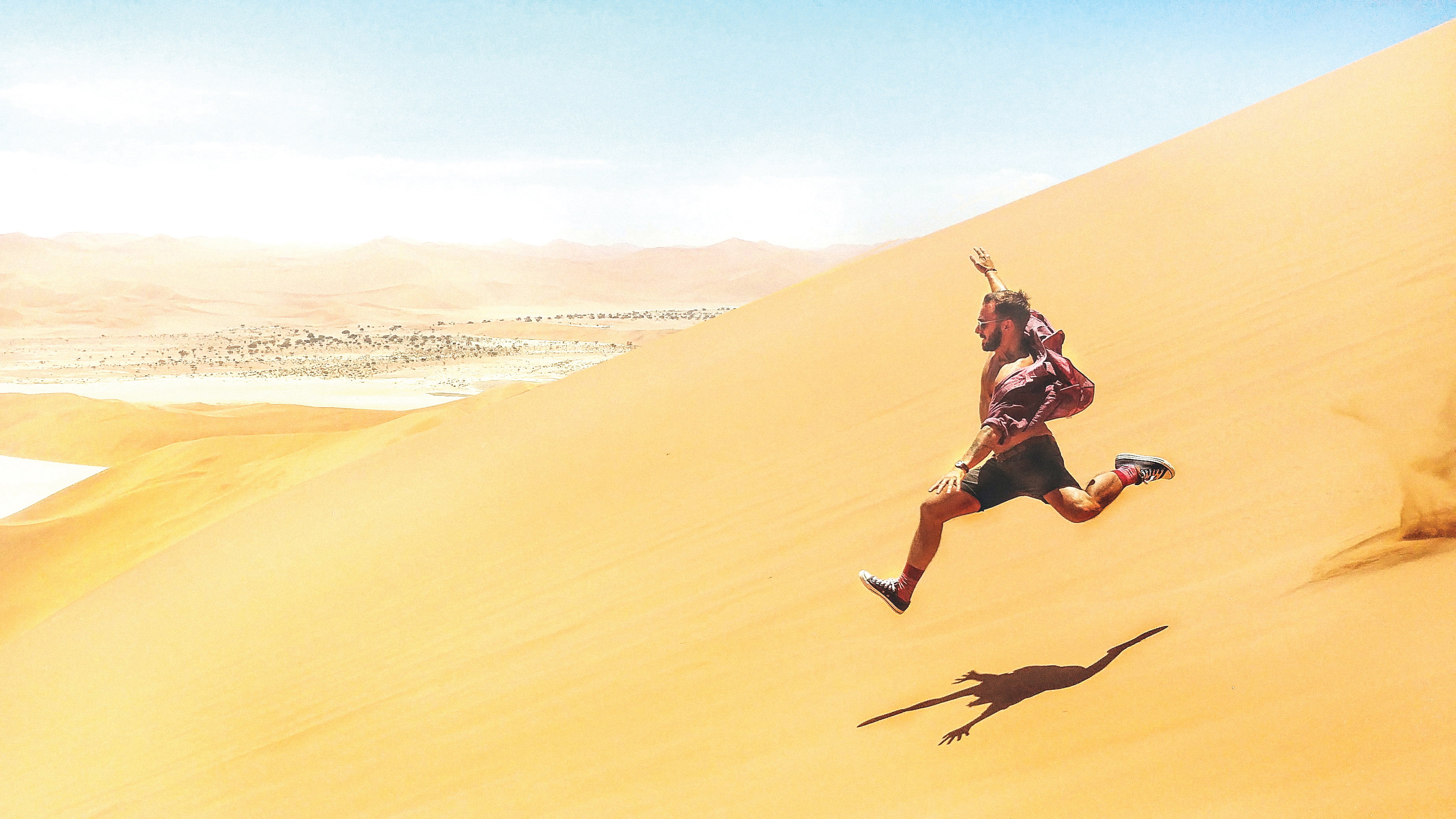 A young male traveller sprints down a steep orange sand dune in Sossusvlei, Namibia
