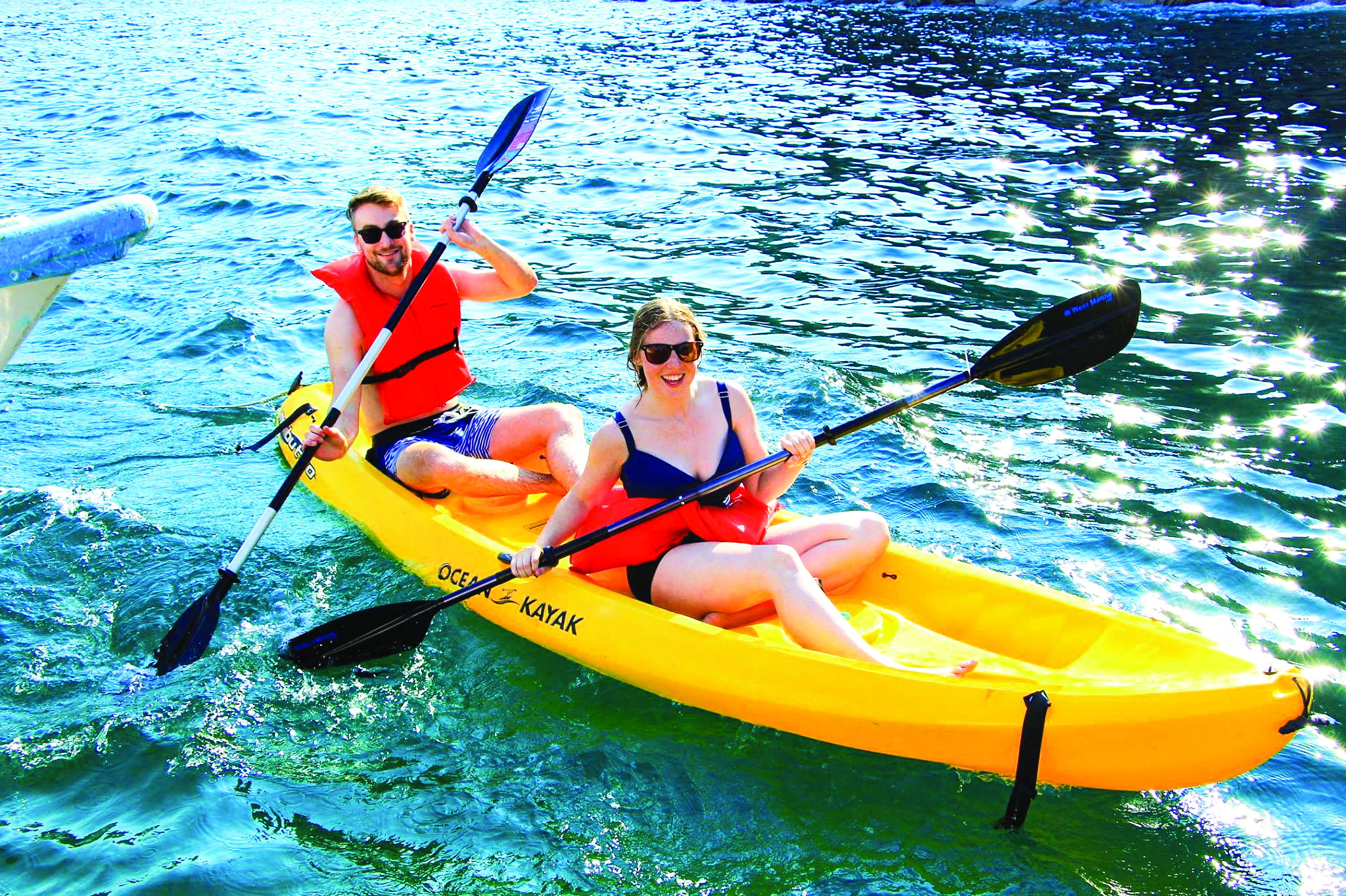 A male and female smile from a yellow kayak in the ocean of the galapagos islands