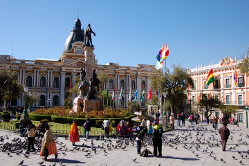 The Palacio del Congresso, or House of Congress in Plaza Murillo in La Paz on a bright sunny day, behind the square's statue and waterfall with pigeons and locals - including bowler hated Aymara women - in the foreground