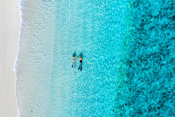 Aerial of a couple snorkelling in turquoise waters along the white sand shoreline, Great Barrier Reef, Queensland. 