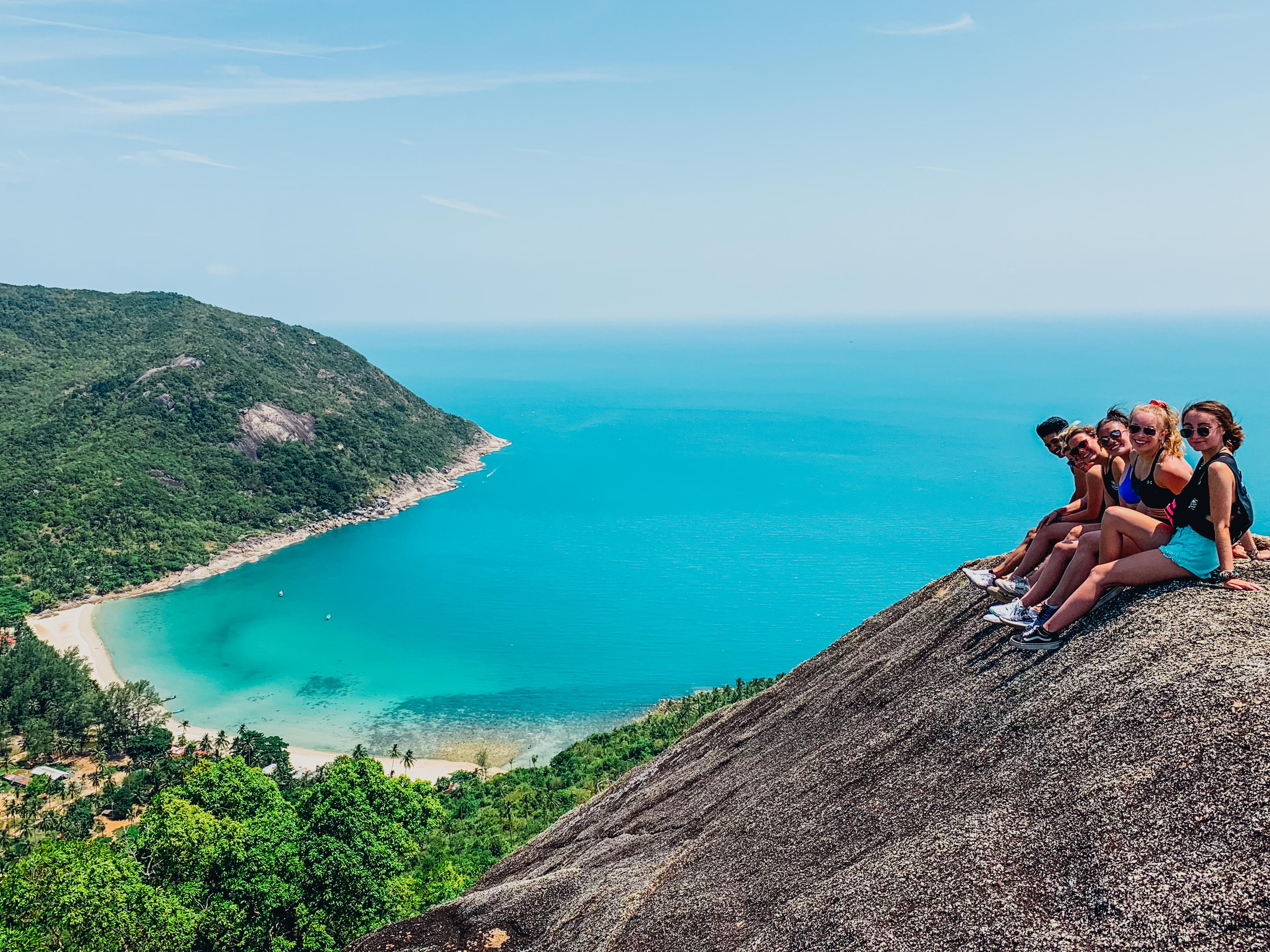 Three travelllers lounge in inflatable tubes with a beer, looking out at jungle clad limestone karst mountains rising from the ocean in front of them.