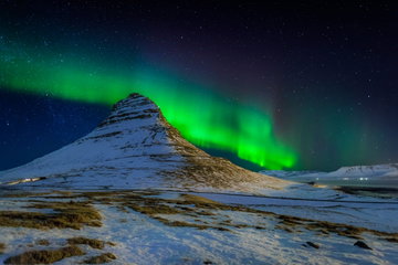 Kirkjufellsfoss Mountain, Iceland in winter with the green glow of the Northern Lights in the background.