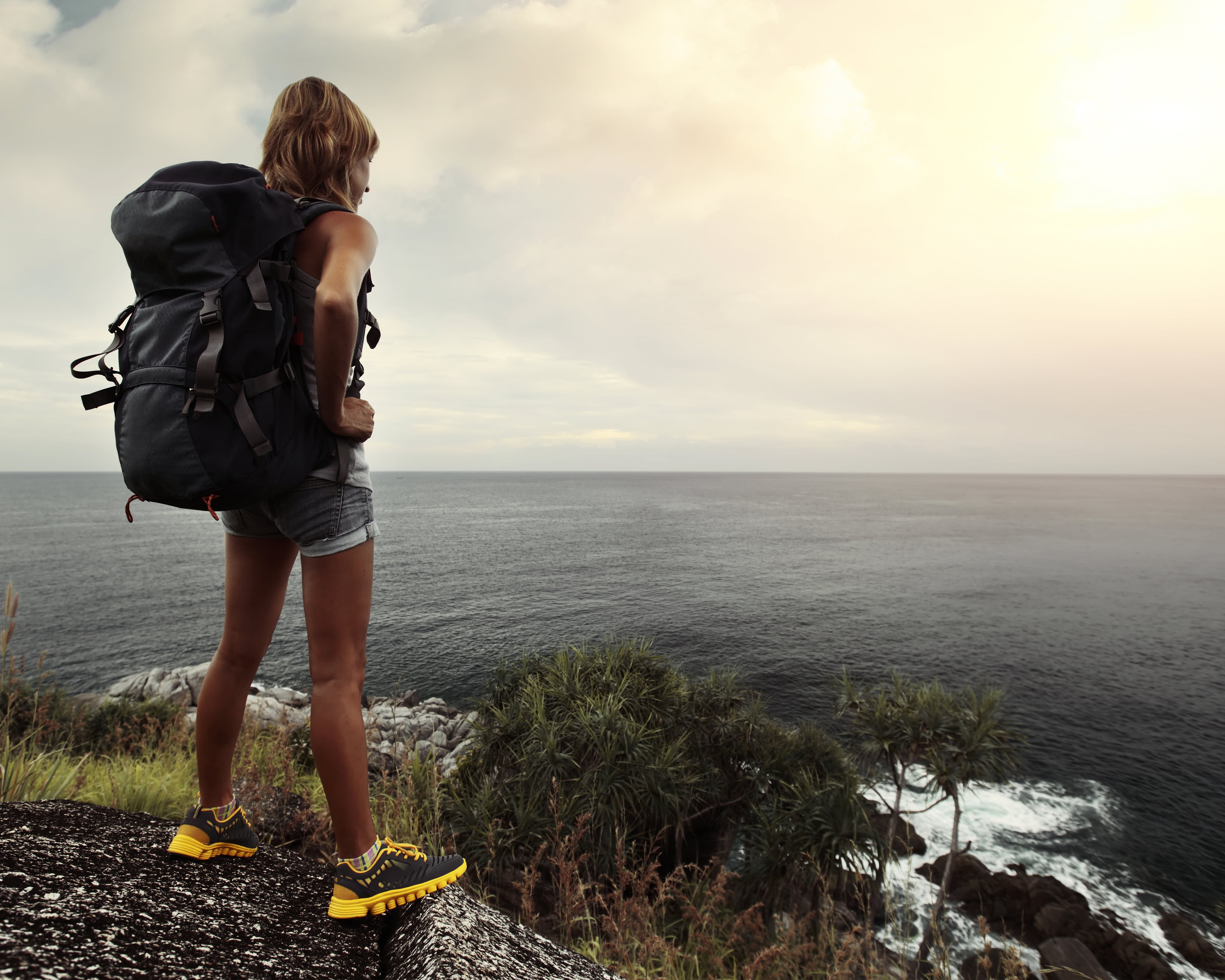 Young tourist with backpack standing on top of a hill and looking to a sea
