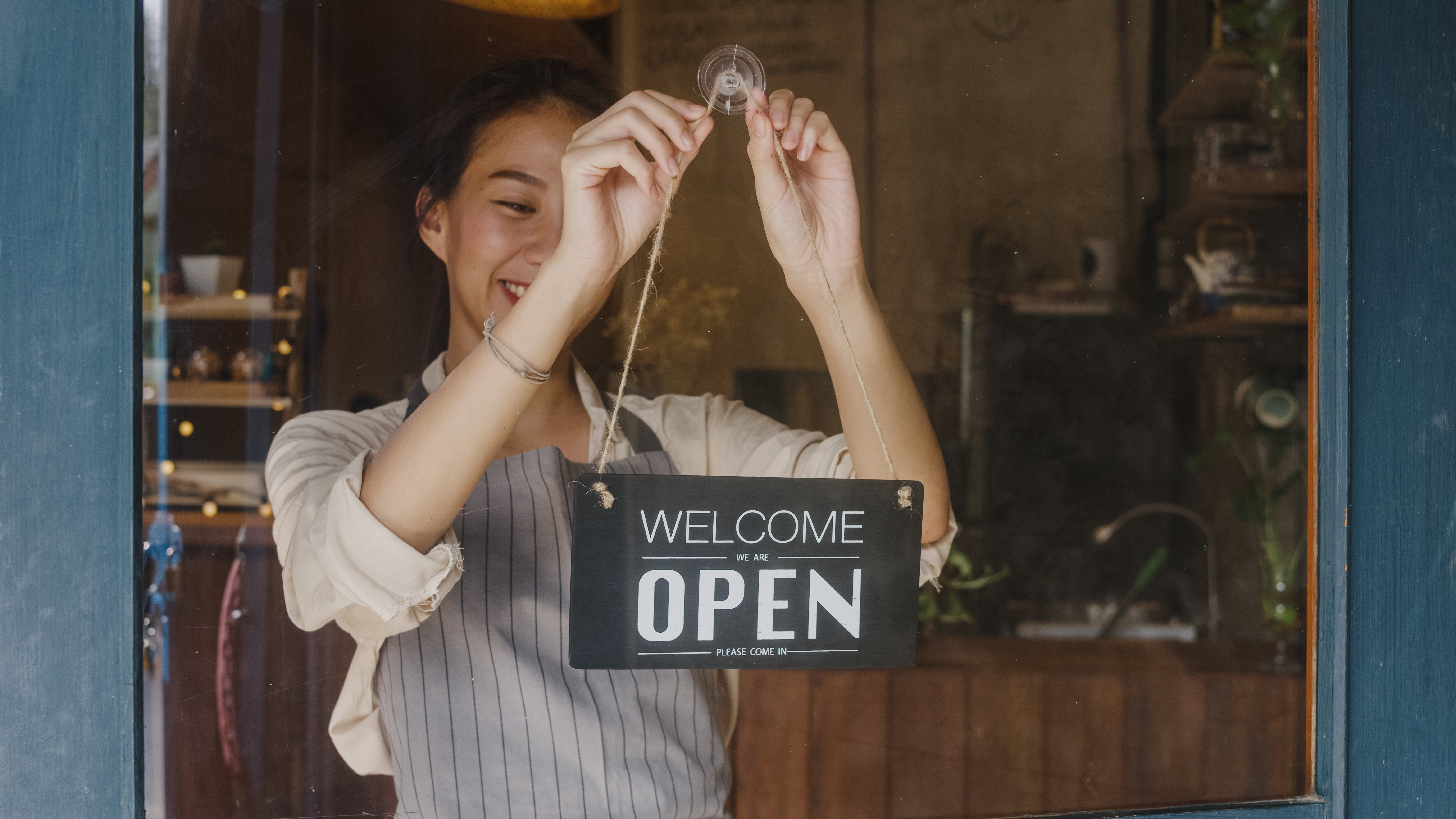 Young Asia manager girl changing a sign from closed to open sign on door cafe