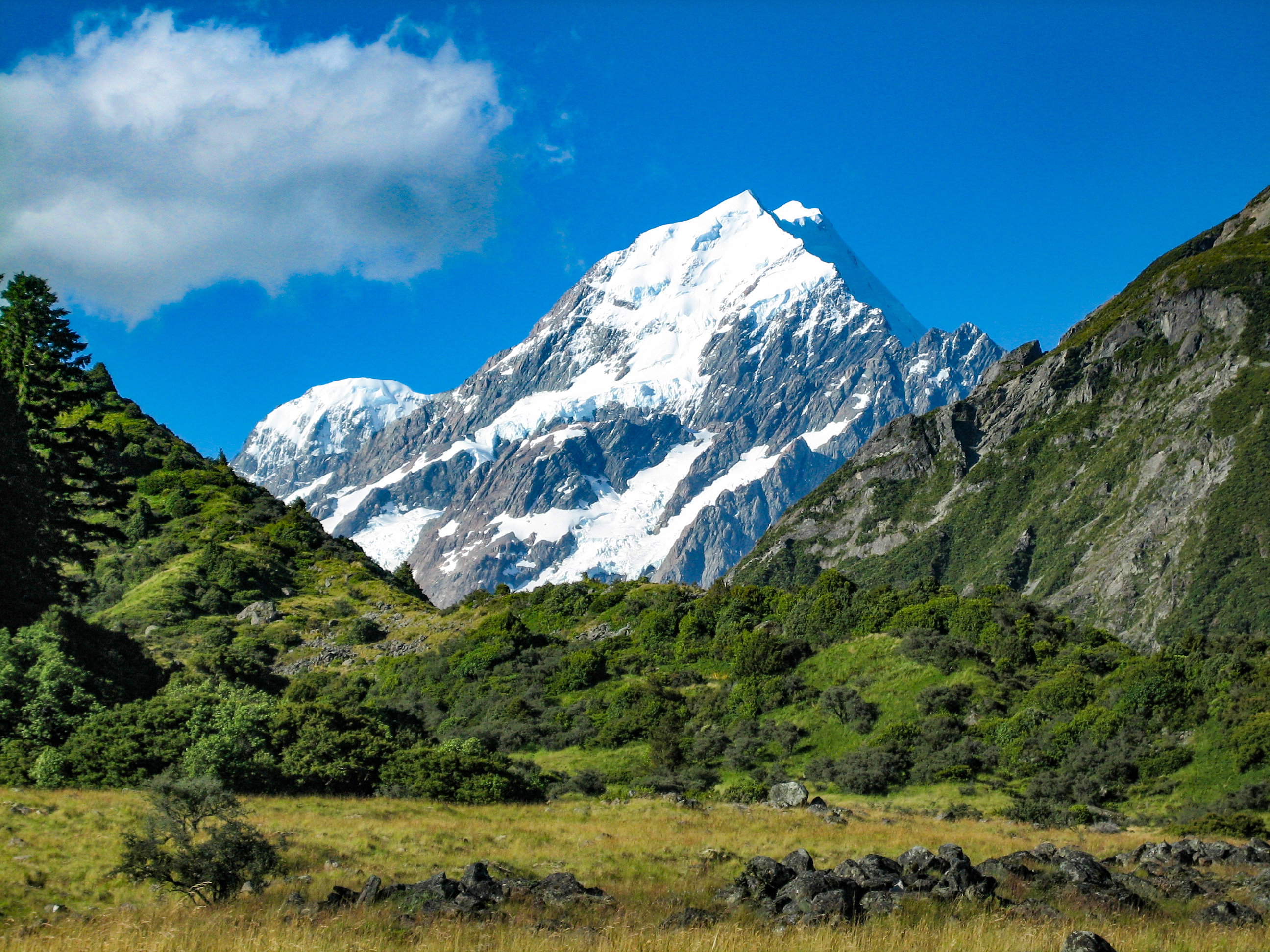 View of snow-capped Mount Cook, New Zealand against blue skies cutting through the mountainous landscape.