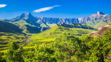 The dramatic mountain range of the Drakensberg Amphitheatre, lush green mountainside and blue sky, KwaZulu-Natal, South Africa