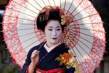 A Geisha in traditional dress standing in the street in full make up holding a umbrella in Kyoto, Japan