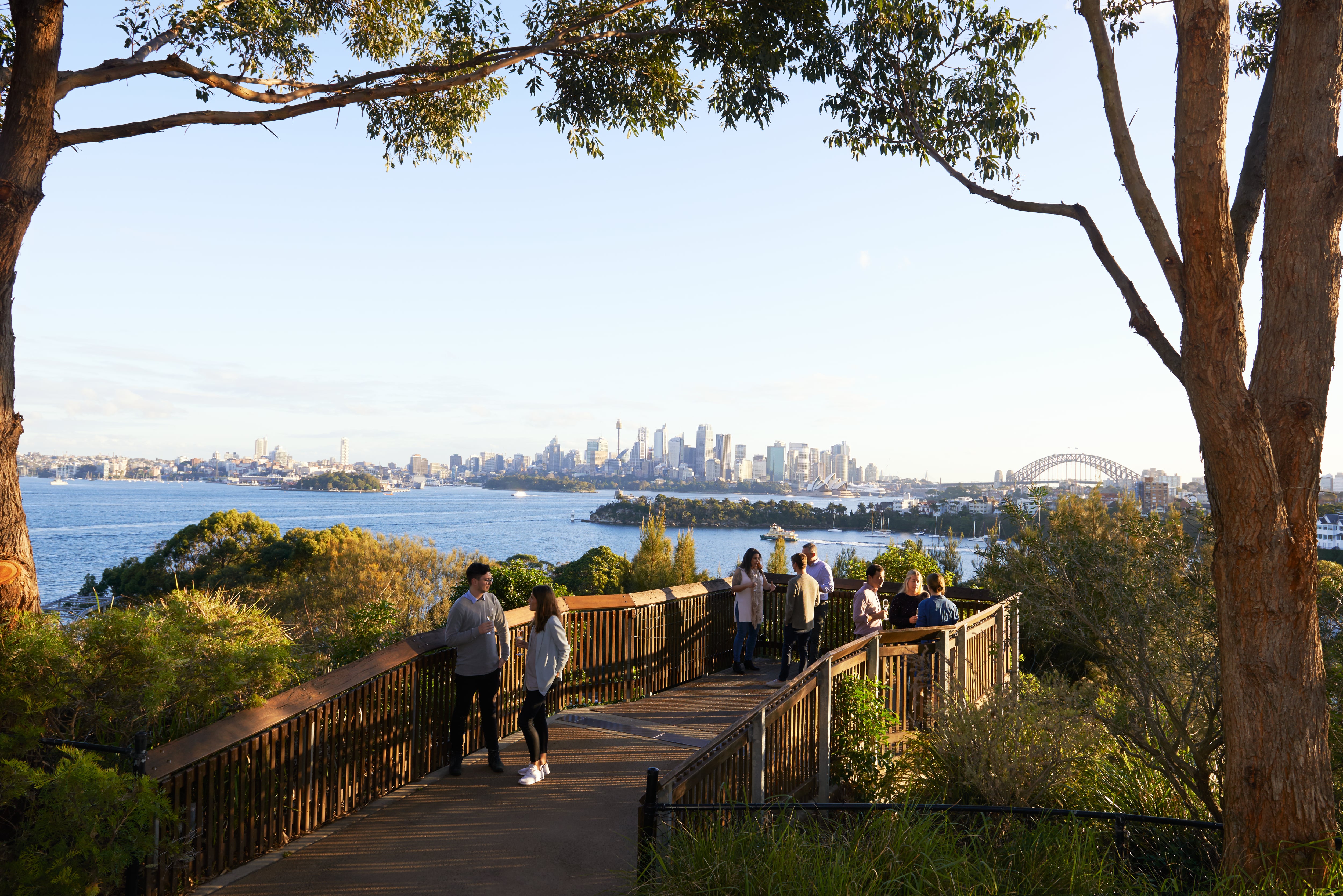 People mingling on a bridge looking out to the Opera House, Harbour Bridge and skyline, on Taronga Zoo Roar & Snore, Sydney, Australia.