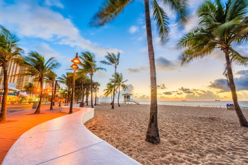 The sun shines down over a long stretch of sandy beach full of beachgoers, the calm ocean lapping up against the shore on a summer’s day on the Atlantic Coast in Florida, USA