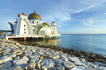 The Melaka Straits Mosque on Malacca Island on a bright sunny day with a rocky shoreline, Malaysia