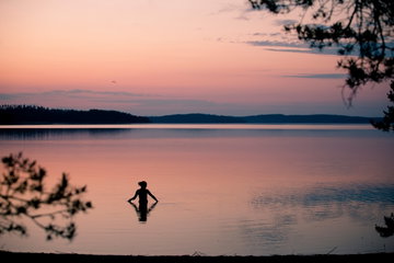 Midnight sun swim in a lake surrounded by forest in Finland