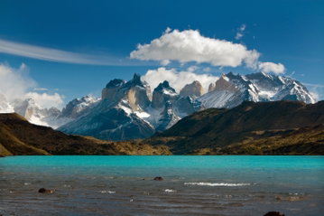 Gentle waves are lapping on a glacial blue lake against a dramatic backdrop of craggy snow-capped, granite peaks in Torres del Paine, Patagonia, Chile