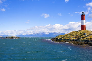 The calms waters of the Beagle Channel stretch out to the snow-capped mountains in the distance, with the iconic Les Eclaireurs Lighthouse standing on the rocky mainland above the waters to the right of the channel