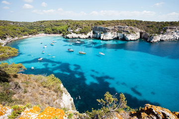 Boats docked on the sea by a rock wall at sunset in Menorca, Spain