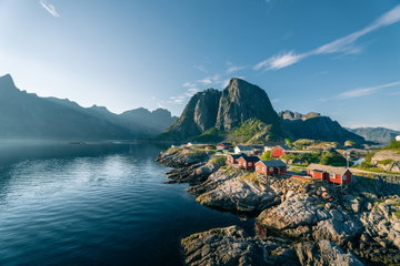 Red rorbu huts by a calm ocean on a sunny summer evening in Lofoten islands, Reine, Norway
