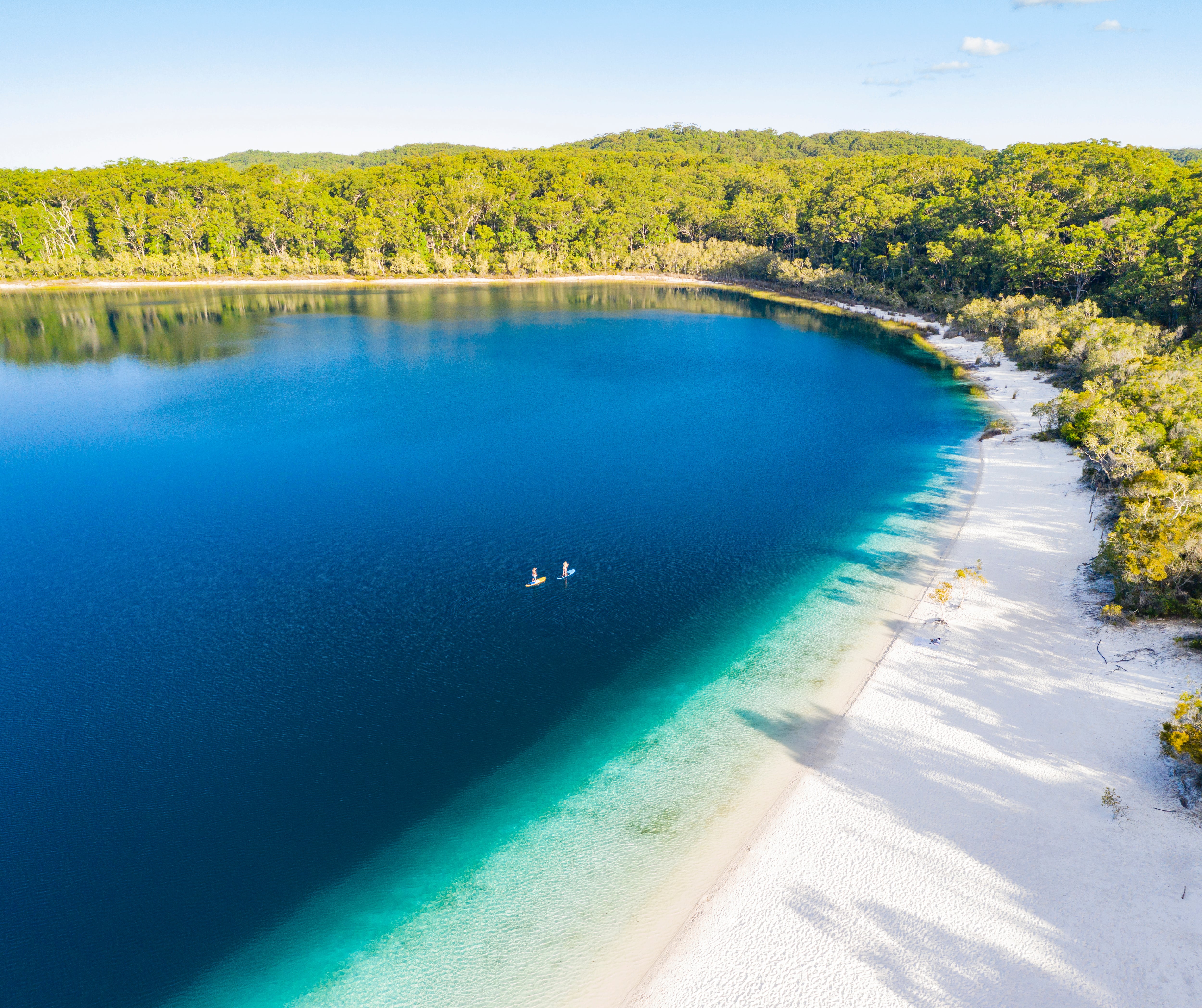 Couple stand up paddle boarding on Lake Mckenzie, Fraser Island, Queensland, Australia