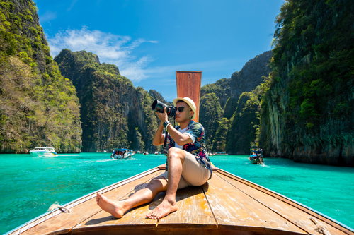 Male tourist taking pictures at the prow of a long-tail boat on a tropical island, Koh Lipe, Andaman Sea, Thailand