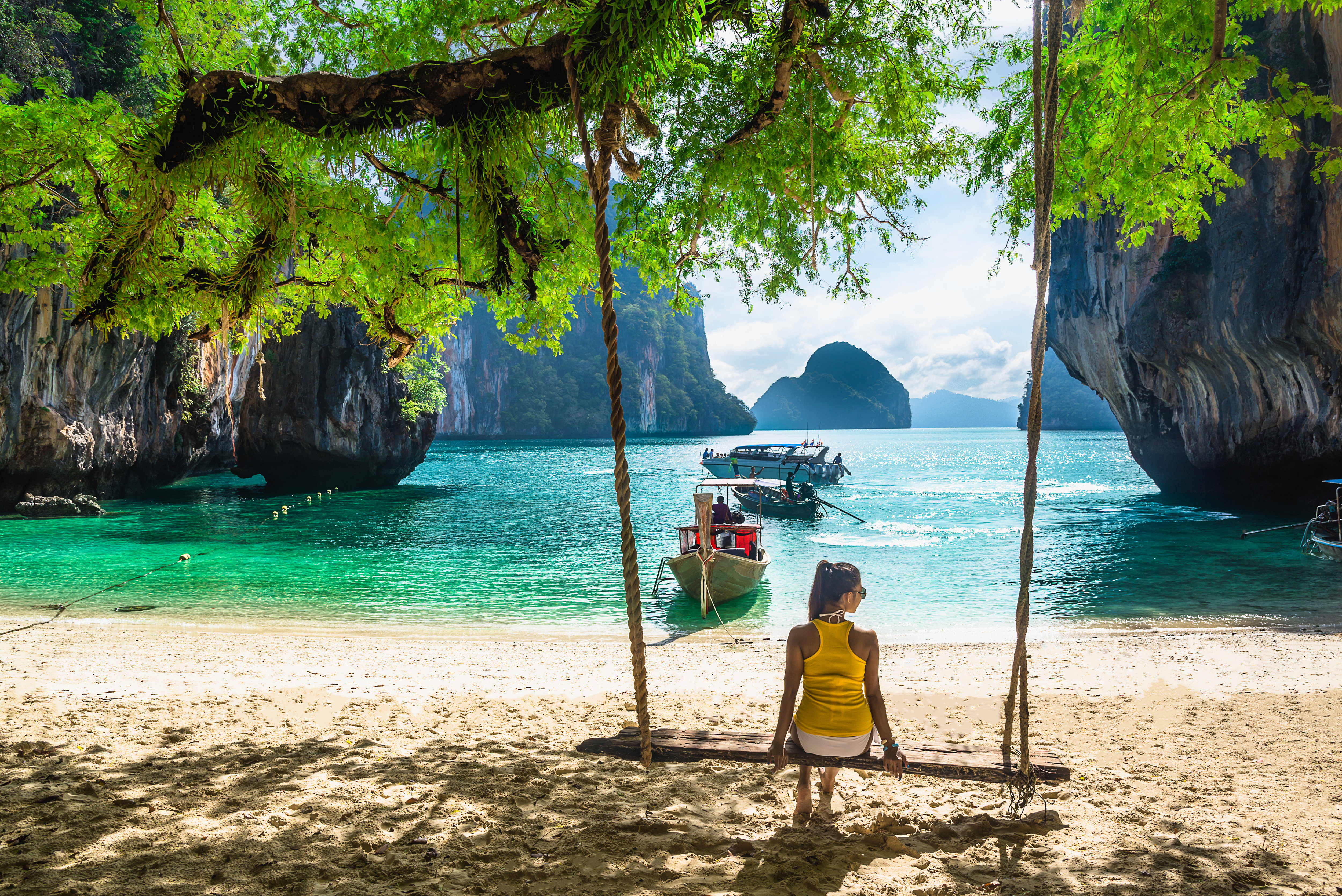 woman in bikini relaxing on wooden swing under tree on tropical beach, Koh Lao Lading island, Andaman sea, Krabi province, Thailand