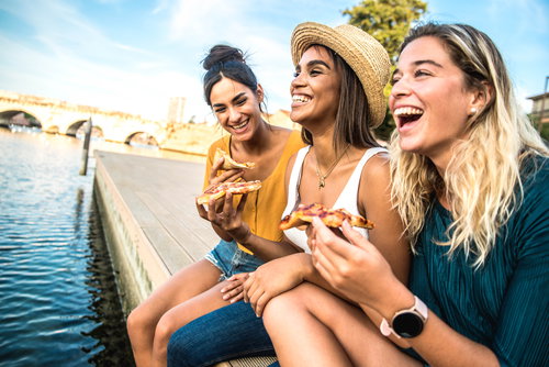 Three young female friends sitting outdoor and eating pizza, Italy