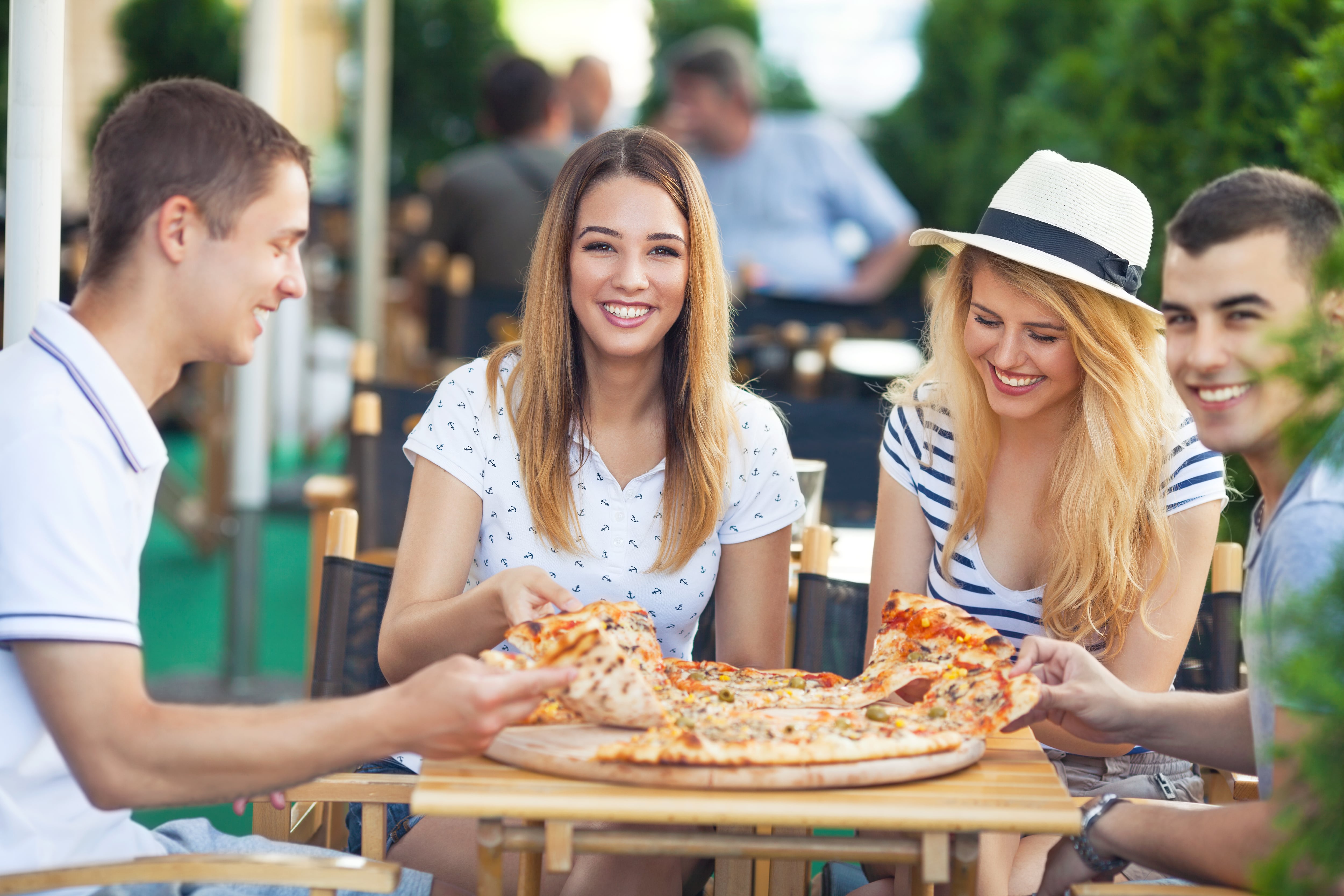 Group of cheerful teenage friends sharing pizza in a outdoor cafe, Italy