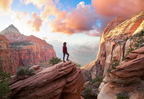 Adventurous Woman at the edge of a cliff is looking at a beautiful landscape view in Zion National Park, Utah