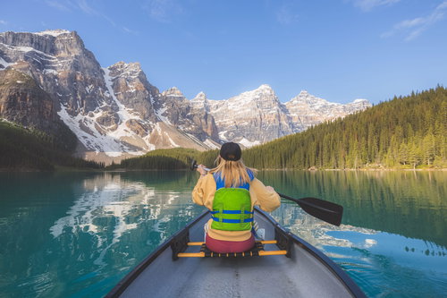 Young woman paddles a canoe on the scenic, picturesque glacial Moraine Lake, Banff National Park