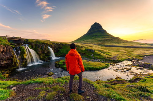 Rear of traveler man in red jacket standing with sunrise over Kirkjufell Mountain, Kirkjufellsfoss Waterfall, Snaefellsnes Peninsula, Iceland