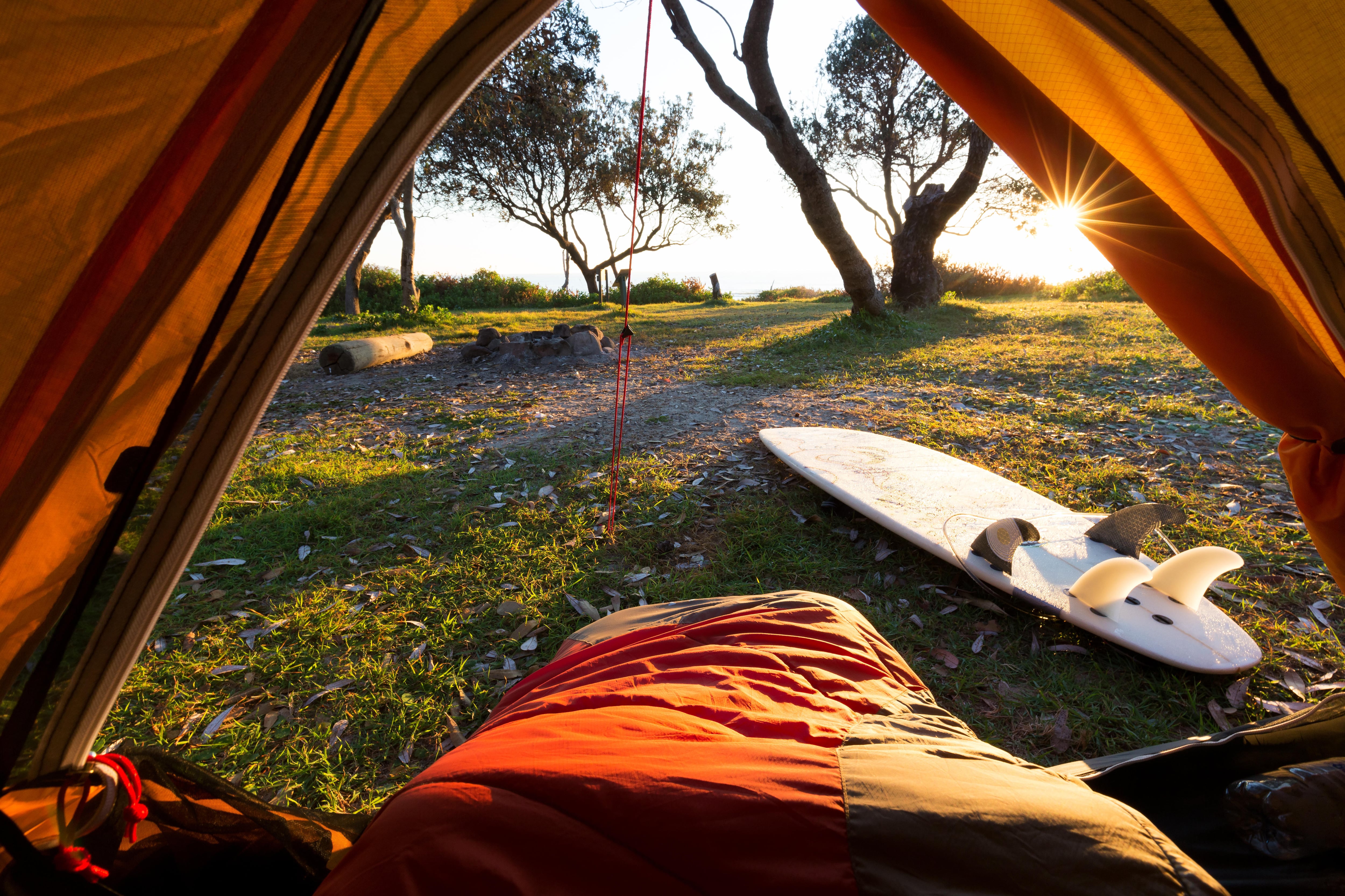 Person in a sleeping bag with a beautiful point of view from a tent as morning light illuminates the campground and surrounds, Australia