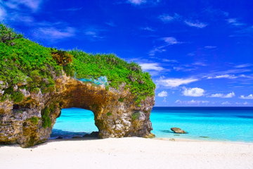 A green, rocky headland overlooking the tranquil sea with a tropical storm in the background on an island in Okinawa, Japan.