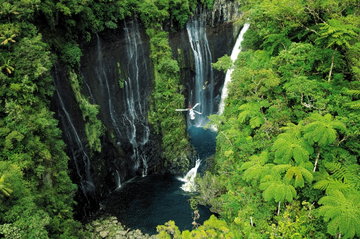 Aerial view of a lush valley in Reunion featuring a cliff dotted with waterfalls cascading into the crater below.