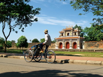 A man riding a cyclo drives past the impressive entrance and walls to Hue Citadel Vietnam with blue sky overhead