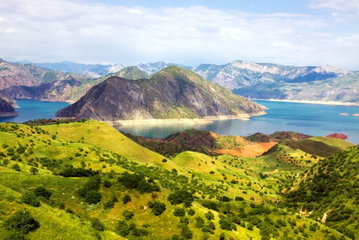 Beautiful green, rolling hills lead down to a glistening lake with a large mountainous Island in the middle, Tajikistan