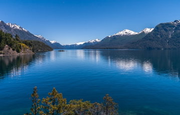 The huge, deep blue Nahuel Huapi Lake in Bariloche, Argentina, taken from near the lakes edge with snow-capped mountains surrounding the lake on either side