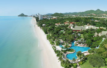 A beautiful resort style swimming pool sits beside a golden beach with the blue water lapping the shore, Hua Hin Thailand