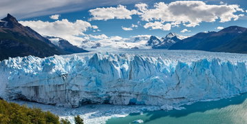 Panoramic view of the face of the colossal Perito Moreno Glacier, Argentina with fallen icebergs in the waters below and mountains surrounding the glacier