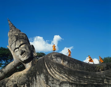Four young monks on top of the Reclining Buddha statue at Buddha Park (Wat Xieng Khuan), Vientiane, Laos.