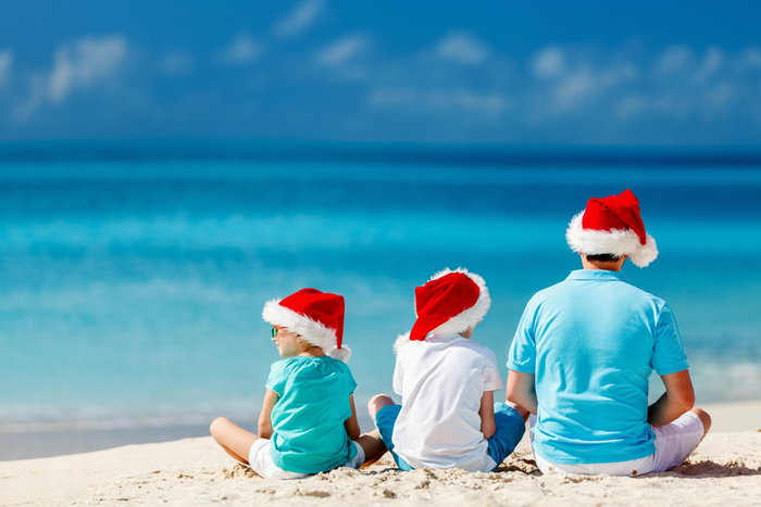 Back view of father and kids wearing red Santa hats enjoying beach vacation on Christmas