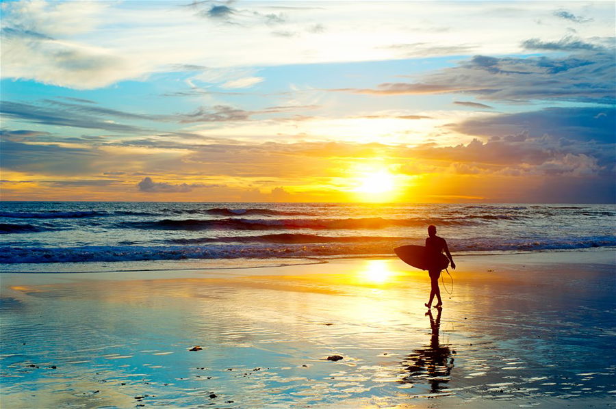 A surfer stands and looks at the sunset on Seminyak Beach, Bali