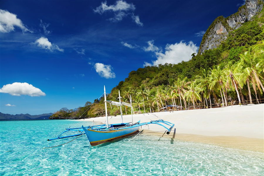 A lone boat sits on the shoreline of the beautiful El Nido Beach in the Philippines